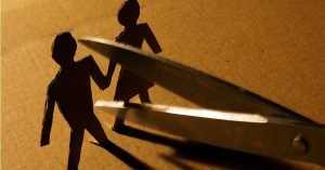 A pair of scissors cutting apart a cardboard man and woman holding hands.